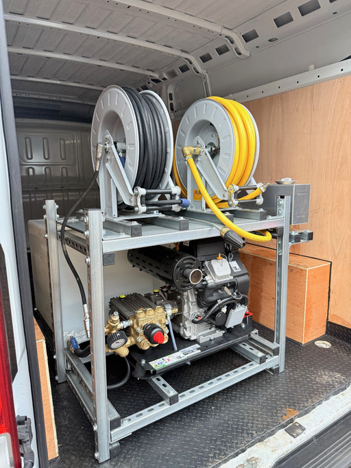 A petrol pressure washer mounted on a metal rack inside a vehicle, with black hoses and various components visible.